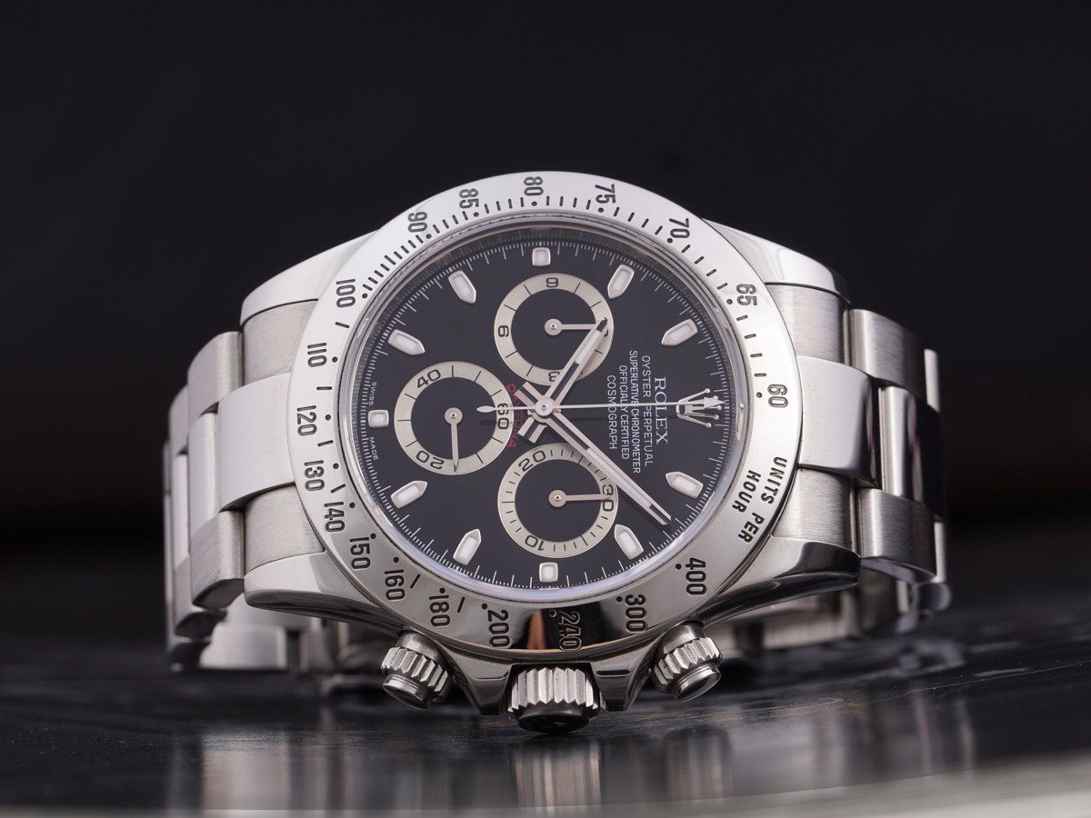 Steel Rolex Daytona with black dial on a dark reflective surface